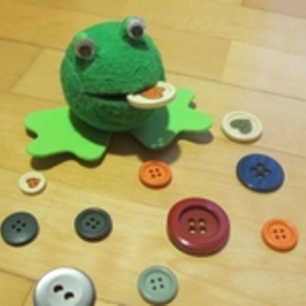 Frosch selbstgebastelt / @ Spiegel OÖ grüner Frosch mit Knopf im Maul, weitere Knöpfen liegen verstreut daneben